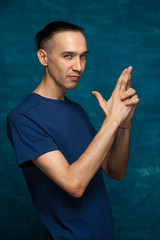 Portrait of young stylish hipster guy wearing glasses showing his fingers as gun and looking at the camera on blue background