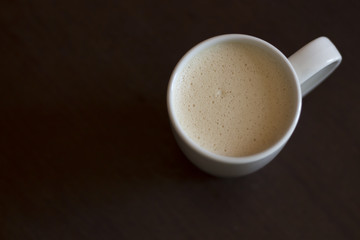 Cappuccino in a white cup on a brown wooden background, top view, copy space