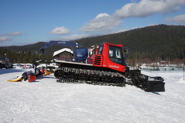 Snow-cleaning bulldozer, for cleaning the ski slope, stands at a mountain ski resort Mountain Salanga in sunny weather, waiting for a snowfall. Kemerovo region. Siberia, Russia