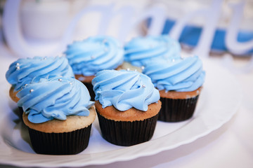 muffins decorated with blue cream and pearls stand on a tray