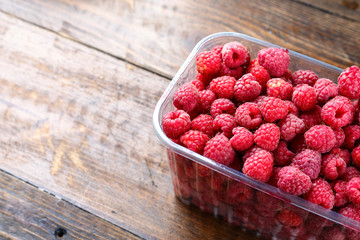 fresh raspberries in a plastic container on a wooden background © alexshyripa