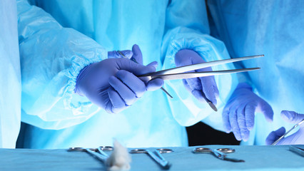 Surgeons hands holding surgical scissors and passing surgical equipment, close-up. Health care and veterinary concept