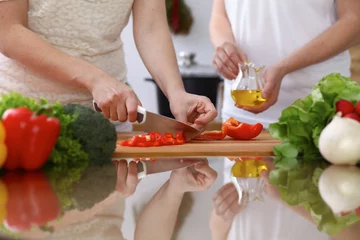 Fotobehang Closeup of human hands cooking in kitchen. Mother and daughter or two female cutting bell pepper for fresh salad. Healthy meal, vegetarian food and lifestyle concepts © rogerphoto