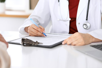 Close up of a female doctor filling up  an application form while consulting patient