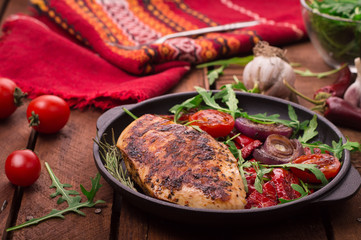 Grilled chicken breast with green salad from arugula and vegetables on a black pan. Wooden rustic background. Top view