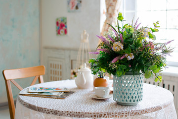 provance interior with table and flowers on it, white cloth and tea set, vase with bunch of flowers standing on the table