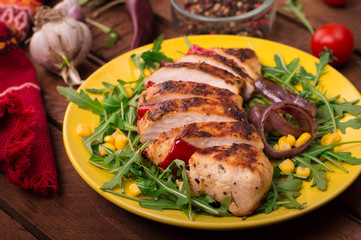 Grilled chicken breast with green salad from arugula and vegetables on a yellow plate. Wooden rustic background. Top view