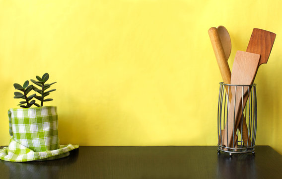 Kitchen Utensils And House Plant On Dark Shelf Over Yellow Wall. Kitchen Interior Background With Copy Space