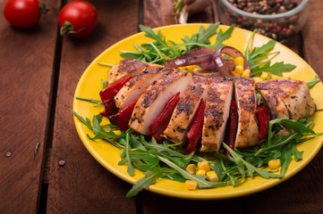 Grilled chicken breast with green salad from arugula and vegetables on a yellow plate. Wooden rustic background. Top view