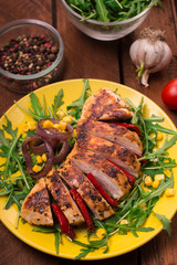 Grilled chicken breast with green salad from arugula and vegetables on a yellow plate. Wooden rustic background. Top view