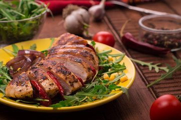 Grilled chicken breast with green salad from arugula and vegetables on a yellow plate. Wooden rustic background. Top view