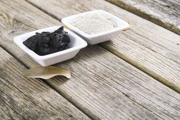 gray cosmetic clay powder and black mud on old wood texture