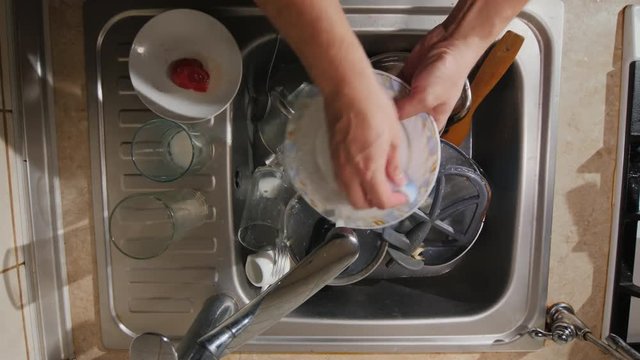 A man washes the dirty dishes in his kitchen, the top view
