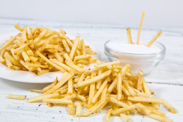 Sticks of french fries and salt on white plate