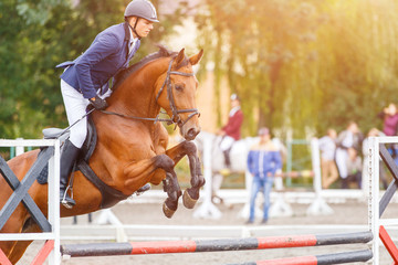 Young rider man jumping on horse over obstacle on show jumping competition