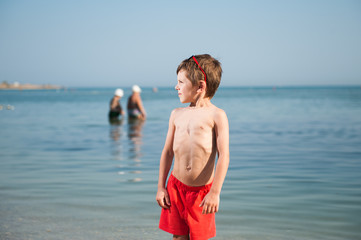 Fototapeta na wymiar handsome health little kid in red shorts on summer beach near sea shore