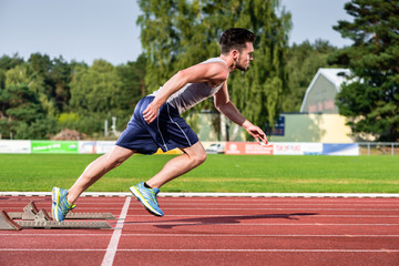 Young athlete on cinder track of sports facility starts to sprint