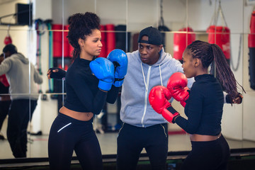 Experienced boxing trainer supervising and teaching two female boxers indoors