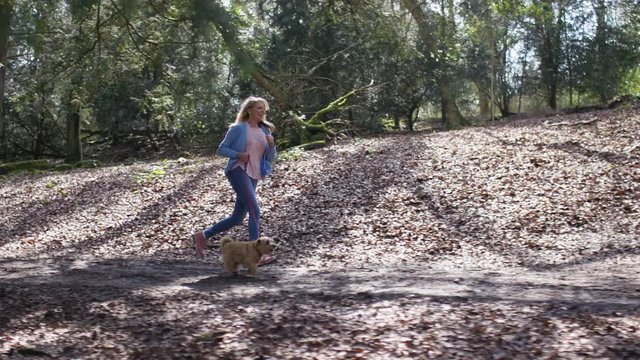 Happy middle aged woman running in the woods with her dog, in slow motion