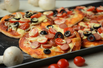 Italian pizza with cheddar cheese, mushrooms, black olives and sausage on white wooden background 