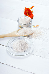 sea clay powder, moisturizer and bath salt with gerbera flower on white wooden table background