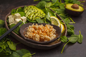 Vegan lunch with brown rice, avocado and tofu on a dark background, vegan food background, top view.