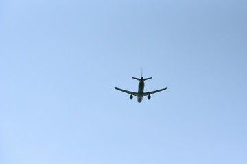 The passenger plane flies away into the blue sky. Back view