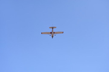 The light airplane flies low overhead on a blue sky background. Bottom view