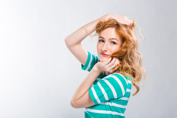 Close-up portrait of a young, beautiful woman with red curly hair in a summer dress with strips of blue in the studio on a gray background. Theme of summer vacation, tourism and summer clothes