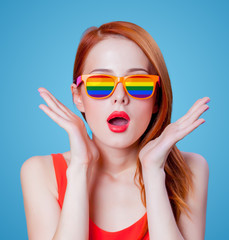 Young redhead girl in rainbow glasses on blue background