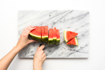 Person cutting watermelon on marble textured cutting board.