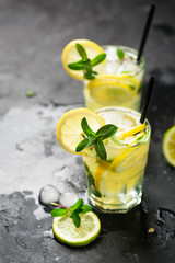 Lemon fruit lime slices caipirinha from Brazil, lemonade mint ice cubes in cold glasses on dark background, alcoholic mojito cockail ice tea green mint leaves, brown sugar spoon, copy space