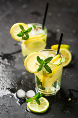 Lemon fruit lime slices caipirinha from Brazil, lemonade mint ice cubes in cold glasses on dark background, alcoholic mojito cockail ice tea green mint leaves, brown sugar spoon, copy space