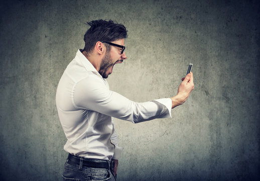 angry man holding smartphone and shouting in anger