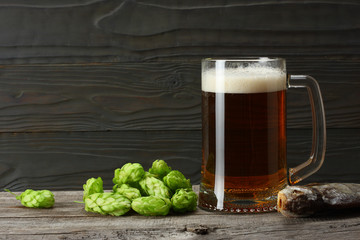 Glass beer with hop cones and dried fish on dark wooden background. Beer brewery concept. Beer background