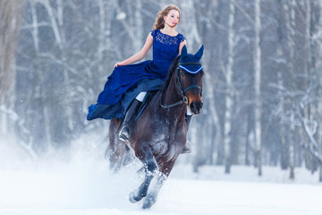 Young girl in blue dress galloping horseback on winter field. Romantic or historical equestrian...