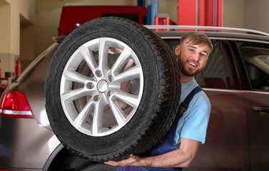 Fototapeta na wymiar Mechanic with car wheel in repair shop. Tire service