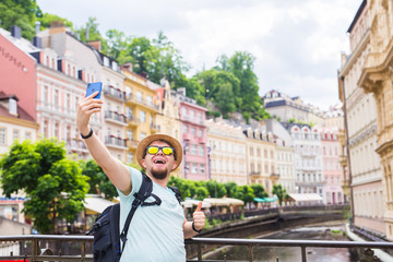 Handsome man taking selfie with mobile smart phone camera in european city. Vacation, travel and holiday concept.