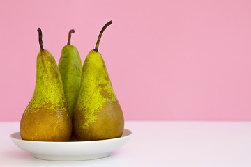 three ripe long pears on a saucer on a creative pink background