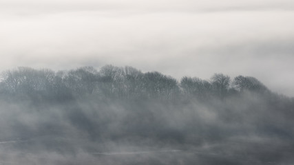 Stunning foggy English rural landscape at sunrise in Winter with layers rolling through the fields