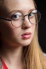 Close up shot of young woman in glasses on a black background.