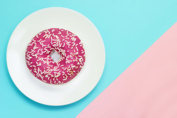 An overhead photo of pink glazed donut with white sprinkles on blue and pink background. Top view. Minimalism, colour contrast on a blue and pink background, donut photo from above in flat style.
