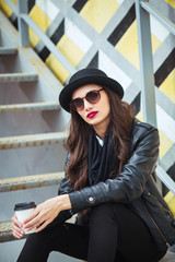 Young stylish woman in a city street sitting and drinking coffee or tea .