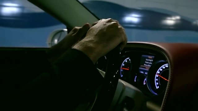 Close up shot of a man's hands on steering wheel in moving car.