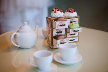 A white kettle, two mugs and cakes