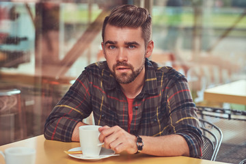 Fototapeta na wymiar A handsome fashionable male with stylish haircut and beard, wearing fleece shirt, drinking coffee at the cafeteria.