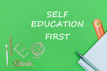 text self education first, school supplies wooden miniatures, notebook on green background