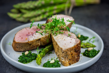 Slices of roasted pork tenderloin on asparagus with pesto from kale and thyme on the white plate....