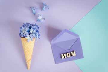 Ice cream horn or cone with purple hyacinth on a purple -mint background. Happy Mother's Day. Floral minimalism geometric patterns greeting card with envelope. Top view, place for text.
