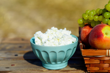 Close up Cottage cheese, and first fruit basket on wooden table over wheat field background. Jewish holiday Shavuot celebration, harvest festival, healthy breakfast, happy sunny day moments concept.